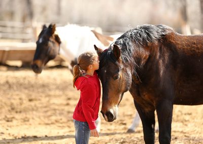 Young Girl whispering into the ear of a brown horse whose head is bent down toward her with a paint horse in background - Lazy L&B Dude Ranch Wyoming