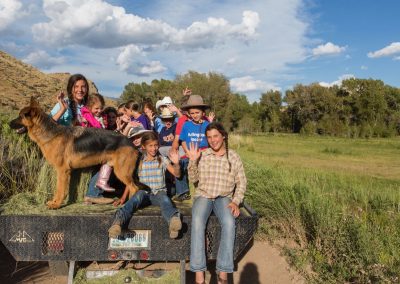 Smiling Children and German Shepherd Dog Sitting on hay bales on the back of a flatbed pickup truck going to a campfire cookout - Lazy L&B Dude Ranch Dubois Wyoming
